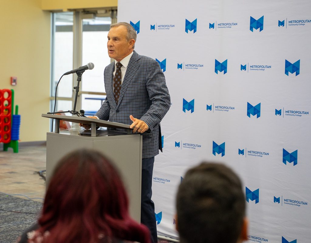 Rob Owen speaks at a podium with a microphone against a Metropolitan Community College photo backdrop.