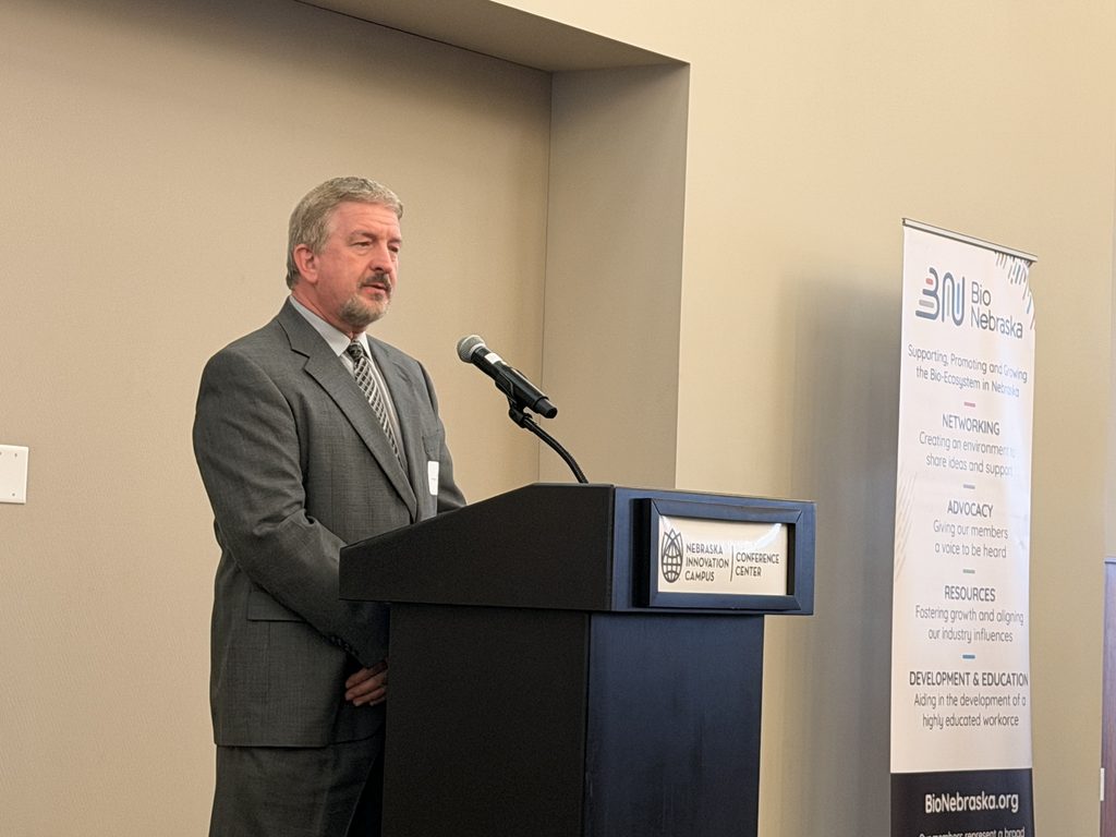 John Poe, General Manager of Phibro Vaccines Omaha, accepts the award. He stands at a podium with a microphone.